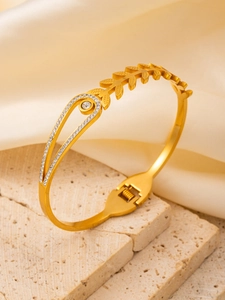 Detail of gold-plated bangle with pavé zircon leaf motif on a textured stone base