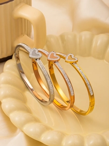 Détail de trois bracelets cœur en acier titane sertis de strass en or, or rose et argent