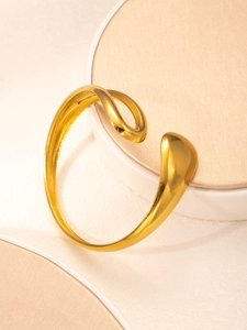 Close-up of golden open cuff bracelet with liquid metal texture on white pedestal