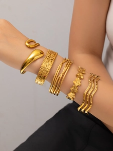 Close-up of stacked 18K gold-plated flower bangles and textured minimalist bracelets