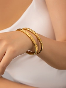 Close-up of dual gold star-engraved bracelets with crystals worn on a wrist