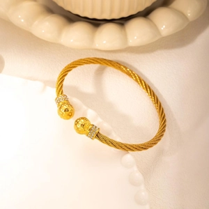 Gold twisted wire rope bangle with pave zircon balls on a minimalist ceramic tray