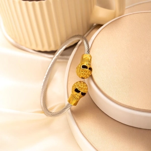 Punk steel cable bracelet featuring dual golden skull accents on a woven metal band