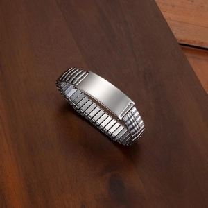 Polished stainless steel stretch watch band ID bracelet for men on a dark wood background