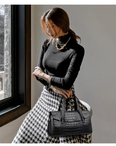 Détail d'un sac à main noir motif crocodile avec doubles anses et pendentif métallique
