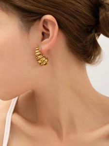 Gros plan de boucles d'oreilles créoles C en titane doré avec un design torsadé chic