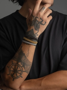 Detailed view of woven metal bangle set in black, gold, and silver on a model's wrist