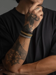 Close-up of three woven mesh cuff bracelets in gold, silver, and black on a tattooed male wrist