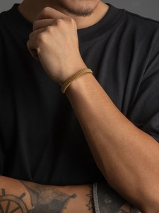 Detailed view of men's golden woven metal cuff bracelet on wrist with textured mesh design