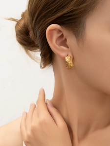 Gros plan détaillé des boucles d'oreilles dorées en C avec gravure texturée de plumes