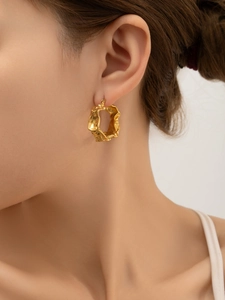 Gros plan de boucles d'oreilles créoles dorées 18k avec texture organique sur modèle