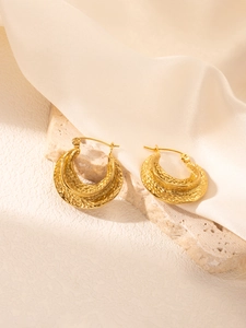 Gros plan de boucles d'oreilles créoles dorées en C avec texture martelée sur soie