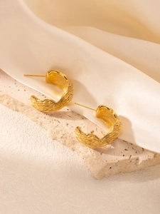 Détail macro de boucles d'oreilles C dorées 18k avec texture ondulée sur pierre