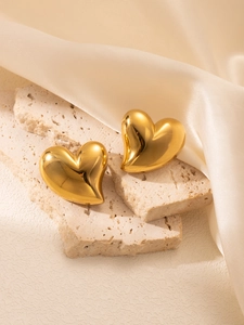 Détail de grandes boucles d'oreilles cœur dorées sur socle en pierre et satin crème