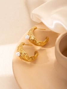 Détail de boucles d'oreilles créoles dorées martelées avec perles sur soie blanche