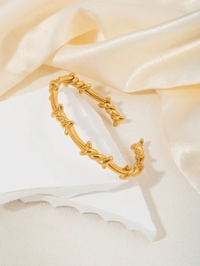 Detailansicht eines goldenen gedrehten Armreifs mit Nietentextur auf Steinboden