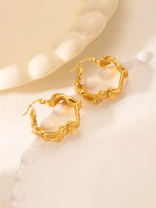 Vue macro de boucles d'oreilles créoles dorées 18k à texture lave sur un plateau blanc