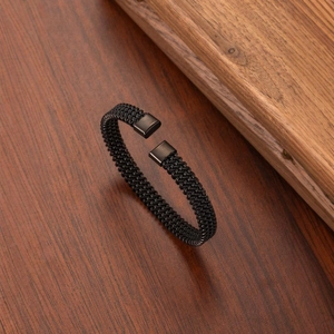 Modern black braided C-shape stainless steel bracelet with matte metal clasp on wood background