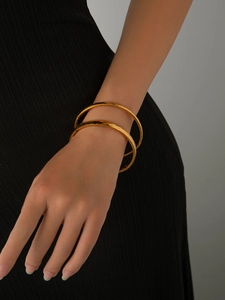 Detailed view of two polished 18K gold-plated titanium steel bangles on a woman's wrist