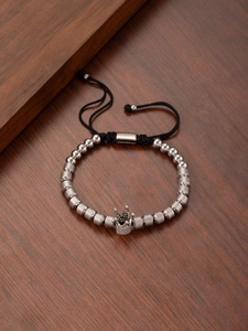 Macro view of woven bracelet with crown charm and textured silver beads on wooden table