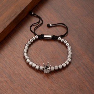 Silver crown charm bracelet with white zircon and black braided rope on wooden background