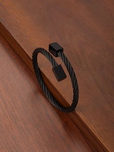 Detail shot of a black wire rope cuff bracelet with square end caps on a dark wood surface