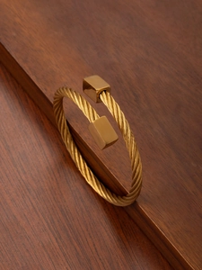 Close-up of gold cable wire twisted cuff bracelet with polished square ends on wood