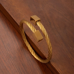 Gold stainless steel twisted cable bracelet with square ends on a rustic wooden background