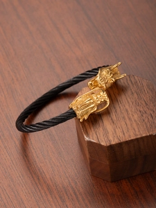Macro shot of 18k gold dragon heads with detailed scales on black steel wire rope bracelet