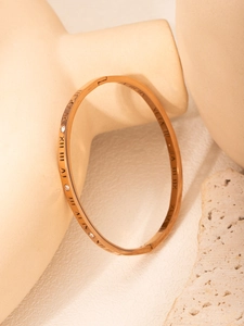 Detail of rose gold roman numeral bangle with zirconia stones on textured background