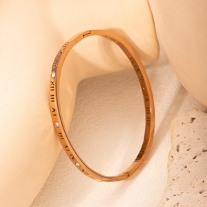 Rose gold titanium bangle with roman numerals and crystals on artistic stone base