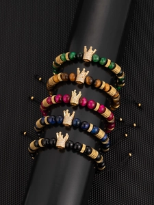 Detailed set of 5 beaded bracelets with gold crown pendants on a black display stand