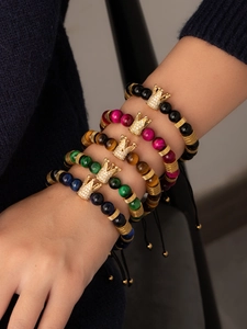 Detail of multi-color beaded bracelets with gold crown charms worn on a wrist