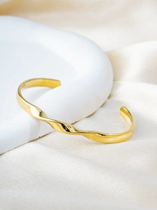 Macro view of polished 18k gold plated Mobius twist bangle on white silk background