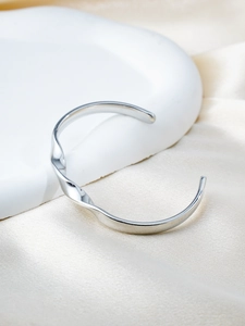 Macro detail of silver Mobius bracelet with smooth polished finish on silk background