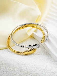 Close-up of gold and silver hugging hands open bangles with intricate engraved patterns