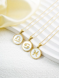 Detailed close-up of 18k gold plated zodiac necklaces with white shell inlay on a stand