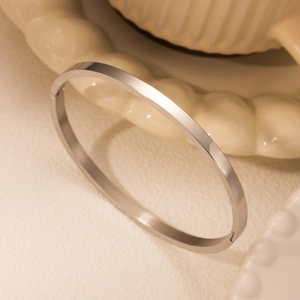 Minimalist silver polished stainless steel bangle on a cream ceramic wave plate