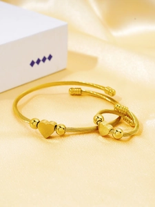 Detail of 18k gold plated twist bangle and heart ring set on golden silk fabric