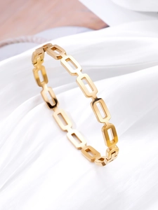 Detailed close-up of hollow geometric gold bracelet on a soft white silk background