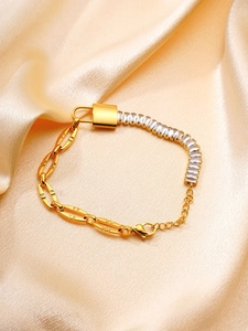 Detailed shot of a gold chain bracelet featuring zircon stones and a padlock charm on satin