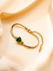 Détail du bracelet en chaîne dorée avec pierre verte en cœur sur satin champagne