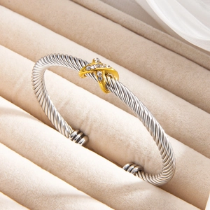 Silver twisted cable open bangle with gold X-shaped diamond-set accent on velvet tray