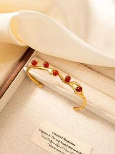 Detail of a wavy 18k gold plated bracelet with red stones in a luxury wooden box