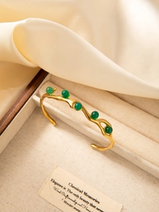 Macro detail of 18k gold plated wave bangle with five vibrant green zircon beads