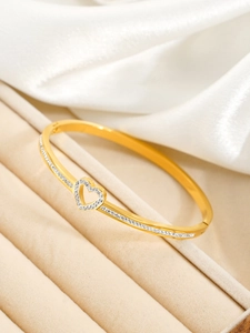 Détail d'un bracelet cœur doré orné de strass blancs brillants sur un fond de soie élégant