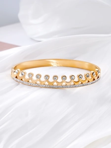 Macro detail of crown shaped gold steel bracelet with sparkling zircons on white silk