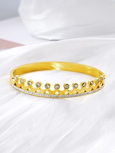 Macro shot of crown bangle with gold plating and sparkling zircon stones on silk fabric