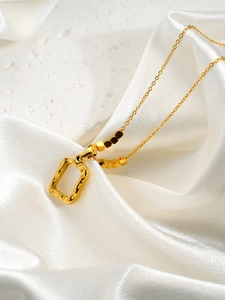 Détail du pendentif carré doré avec texture lave et perles sur tissu en soie