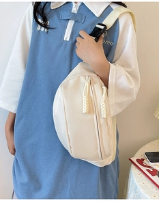 Gros plan d'un sac banane crème avec une large bandoulière tissée sur un mannequin